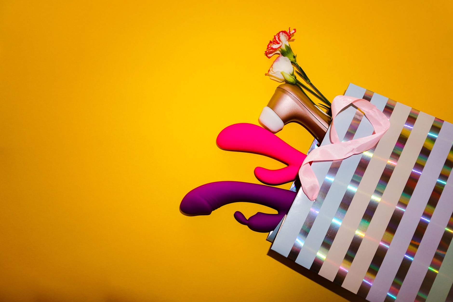 Colorful vibrators with flowers arranged on a bright yellow background, representing pleasure options for solo and partnered play.